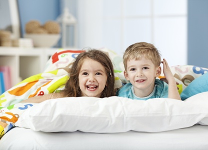smiling girl and boy hiding under bed sheets